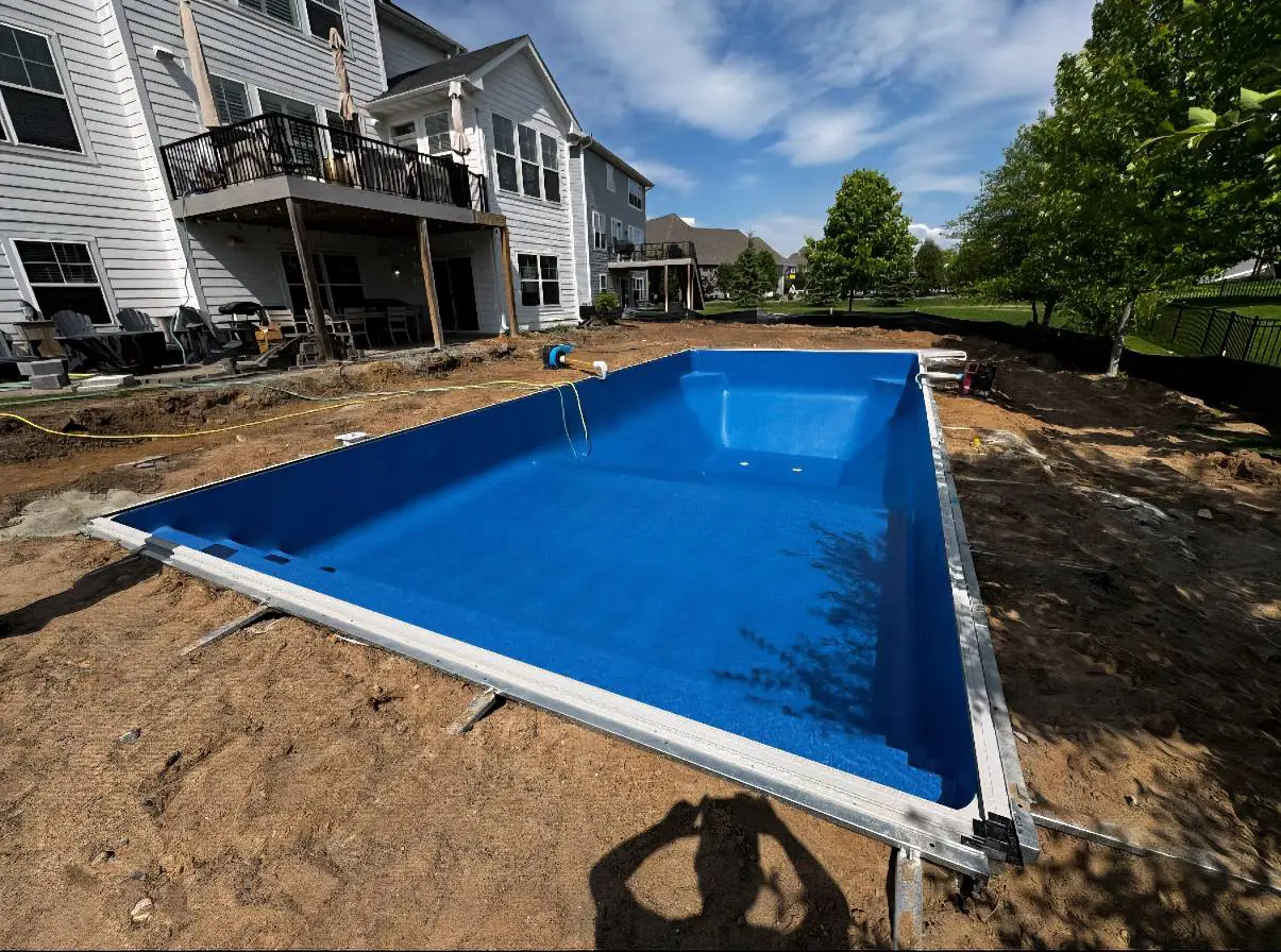 In-ground residential swimming pool in Dellwood, MN, with a bright blue liner freshly installed. The surrounding area is unpaved, with exposed dirt and construction tools visible.