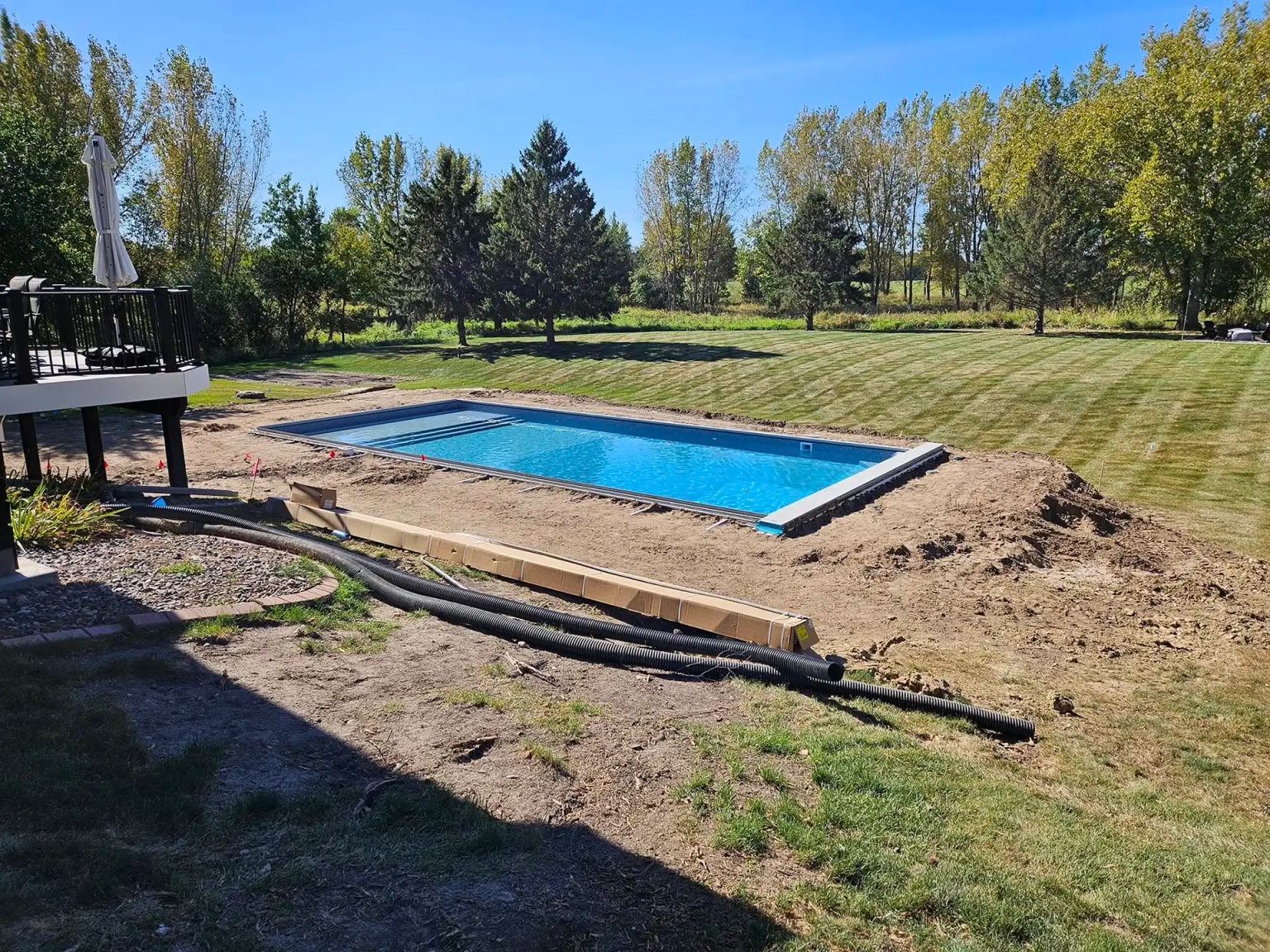 A backyard in White Bear Lake, MN, showing a partially completed swimming pool installation surrounded by fresh soil and landscaping preparations