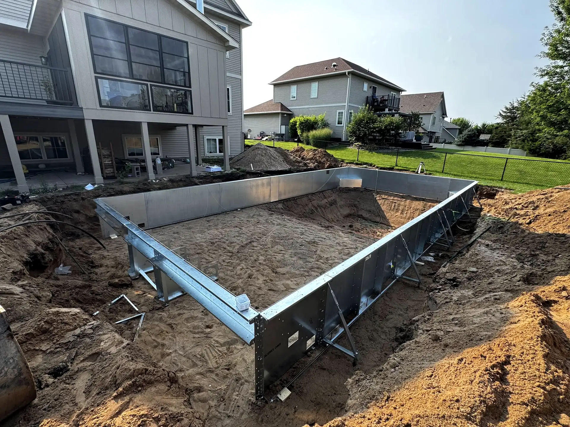 In-ground swimming pool construction in Mounds View, MN, showing a rectangular metal pool frame partially installed in a sandy excavation area.