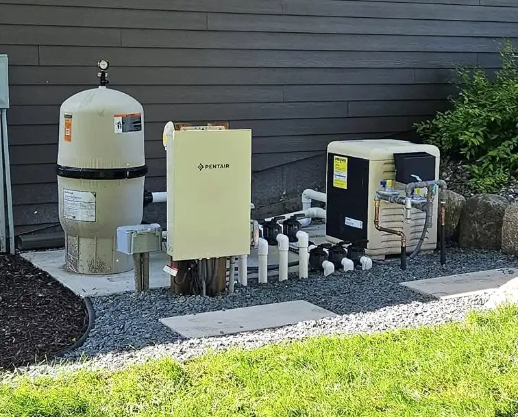 Pool equipment setup on a concrete pad beside a house in White Bear Lake, MN, featuring a beige pool filter tank with a pressure gauge, a pool pump, multiple PVC valves and pipes, and a black pool heater unit.