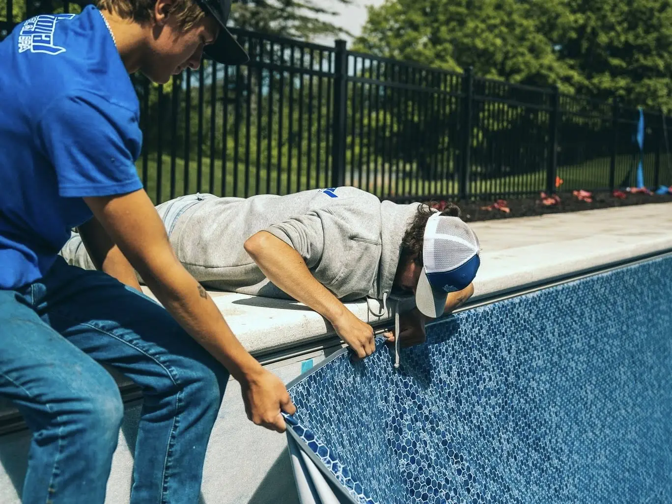 Two workers install a new swimming pool liner with a blue tile pattern in North Oaks, MN. One person holds the liner in place while the other uses a tool to secure it into the track along the pool wall.