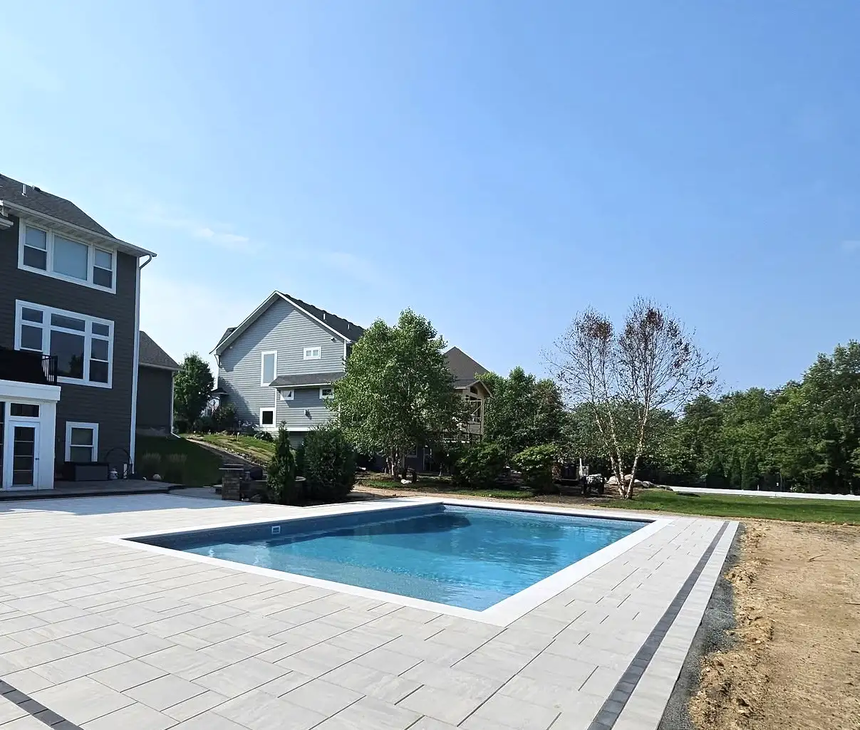 In-ground rectangular pool in a White Bear Lake, MN backyard, surrounded by light-colored stone pavers.