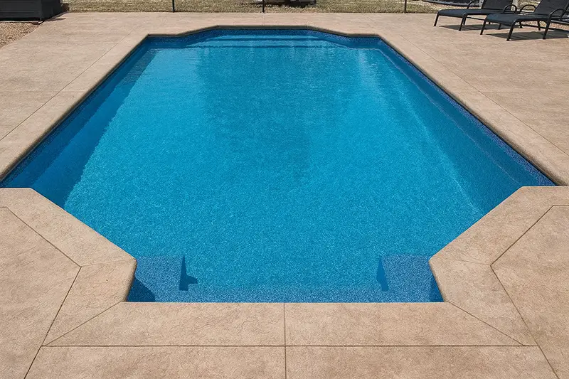 A Grecian-style inground swimming pool with bright blue water, characterized by straight edges and chamfered, inward-angled corners.