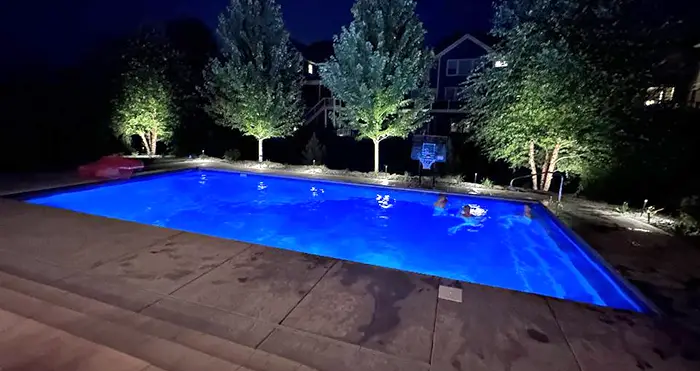 A backyard swimming pool in White Bear Lake, MN glows with vivid blue underwater lighting at night, creating a striking contrast against the dark surroundings.