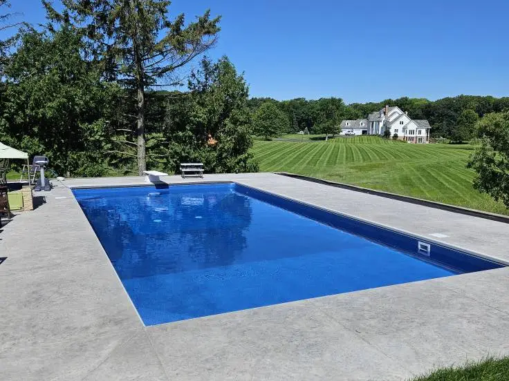 A large rectangular inground swimming pool in Dellwood, MN, with deep blue water, sits in the center of a wide light-gray concrete deck.