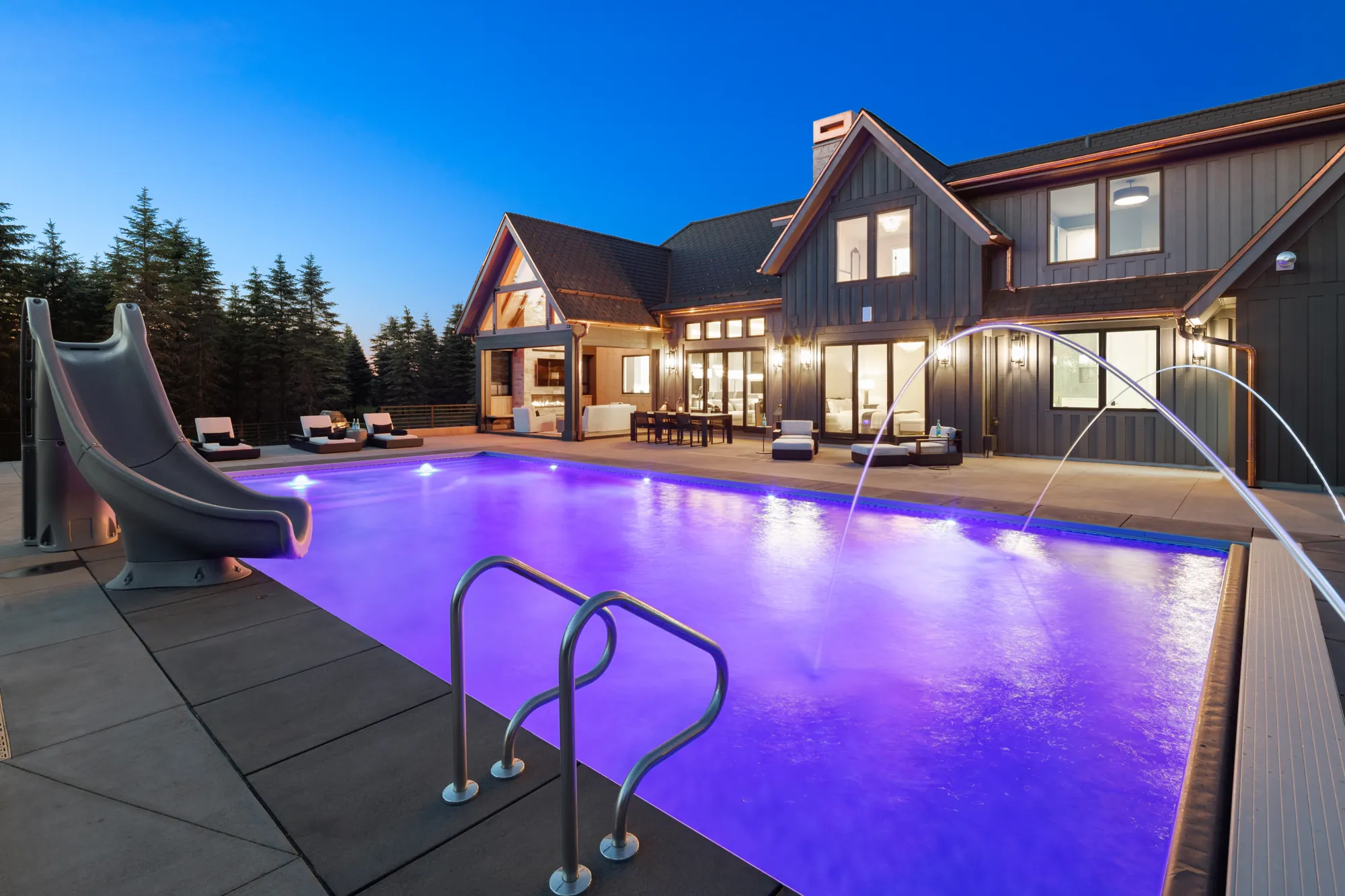 Luxury home in Bayport, MN, with a glowing purple-lit in-ground pool at dusk, featuring a water slide, deck jets, Pentair pool lights, and poolside lounge chairs.