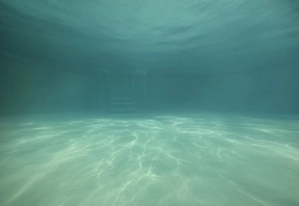Underwater view of a swimming pool with cloudy water, making visibility hazy.