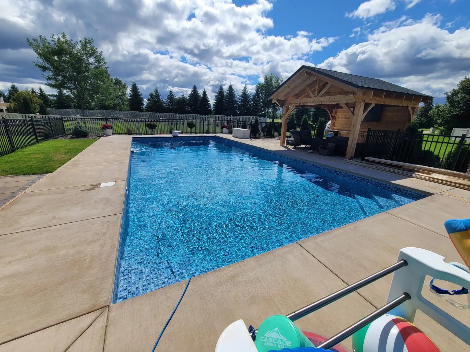 Completed in-ground swimming pool installation with sun deck and backyard pavilion