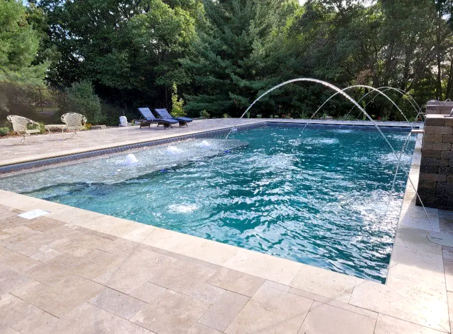 A large rectangular swimming pool in Mahtomedi, MN, with built-in fountains and arcing deck jets spraying streams of water into the pool.